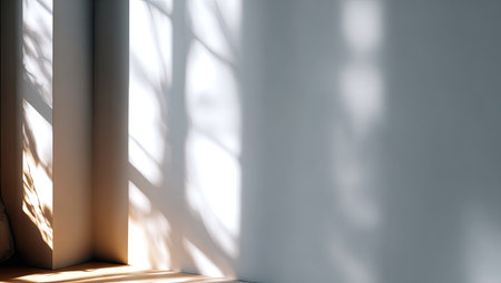 Sunlight streams across a plain interior, casting intricate shadows from unseen objects onto a neutral wall. The composition highlights the interplay of light and shadow, with a focus on geometric shapes and textures. It may be suitable for backgrounds, design elements, and conceptual illustrations. The overall aesthetic is minimalist.の素材