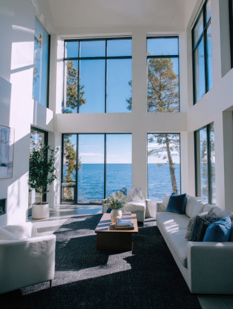 An open-concept living space showcases a stunning ocean vista visible through large windows. The interior features a bright, modern design with white walls and comfortable seating. Sunlight streams in, creating a warm and inviting atmosphere. This image could be used for interior design, real estate, or lifestyle content.の素材