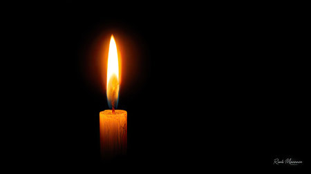 A solitary candle with a bright, warm flame stands out against a black background. The image features a close-up view highlighting the candle's texture and the flame's glow. The lighting is dramatic, emphasizing the contrast. Suitable for various design applications and conceptual projects.の素材