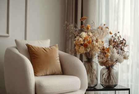 An inviting living space features a modern armchair complemented by decorative dried flowers. Neutral tones dominate the scene, creating a sense of tranquility. Natural light streams through a sheer curtain, illuminating the textures of the cushions and the delicate details of the floral arrangements. This image is suitable for various commercial uses.の素材