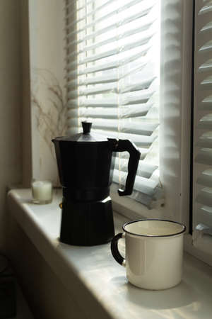 Coffee maker with a cup of freshly brewed coffee on a windowsill in the morning at sunrise