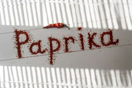 Red paprika with a red inscription on a white table with sunbeams and shadows