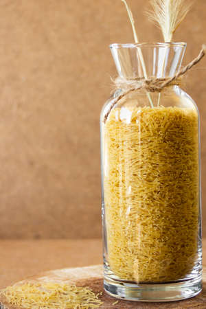 Small vermicelli in a glass jar on a wooden stand, scattered on the table. High quality photo