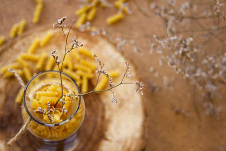 Spiral pasta in a glass jar on a wooden stand, next to it are dry tree branches, on a beige...