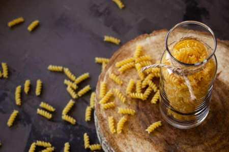 Spiral pasta in a glass jar on a wooden stand, scattered on the table. High quality photoの写真素材