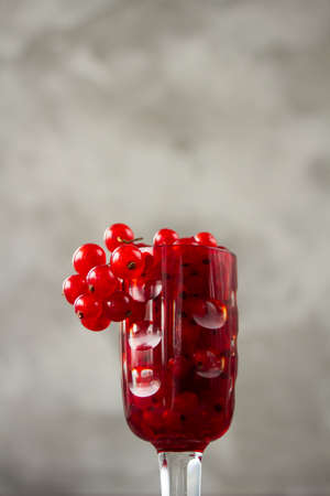 Red currant in a shot glass, the rest is scattered around it on a gray textured background. High quality photoの写真素材