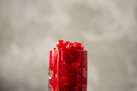 Red currant in a shot glass, the rest is scattered around it on a gray textured background. High quality photoの写真素材