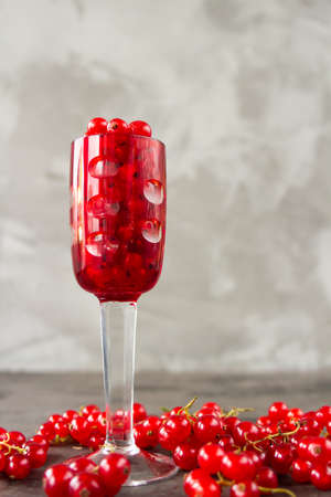 Red currant in a shot glass, the rest is scattered around it on a gray textured background. High quality photoの写真素材