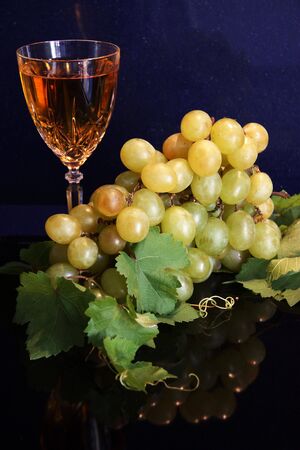 A festive still life of a glass of white wine with a bunch of white grapes against a darl blue marble backdrop.の写真素材