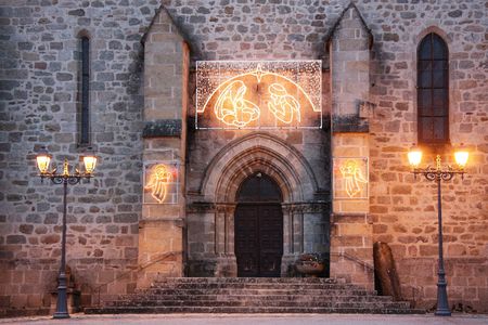 The entrance to an old stone church adorned with shining Christmas lights of the Nativity and angelsの写真素材