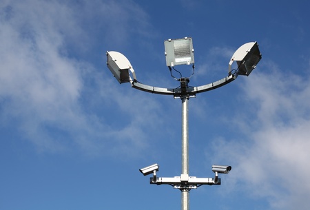 A close up of a  pole with three large square security lights and two security or surveillance...
