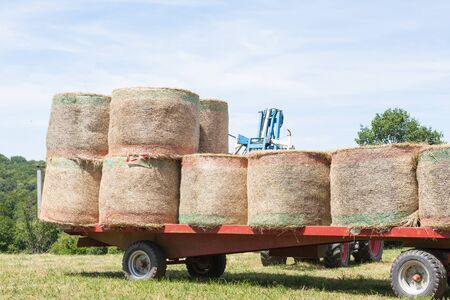 Farmer using a mechanical arm to load and stack round hay bales on a trailer for transport, close up view with bales in the foregroundの写真素材