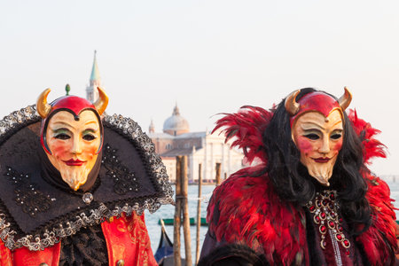 Venice 2017 Carnival, Italy. two men dressed in Satan or devil costumes and masks at the lagoon at San Marco with the church of San Giorgio Maggiore behind. with focus to the one on the left and copy space above in atravel and tourism conceptのeditorial素材