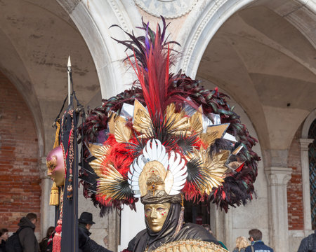 Feb 2017 Venice Carnival, Italy. Man wearing large mask and headdress dressed in a Roman centurion  costume carrying a shield and banner in front of the Doges Palaceのeditorial素材