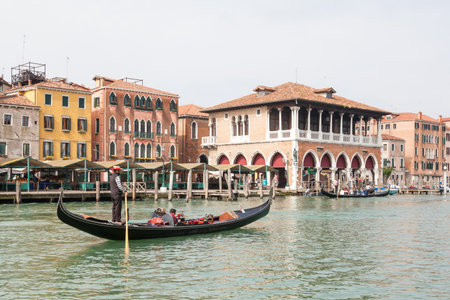 7 May 2017 Venice, Veneto, Italy. Gondolier rowing his gondola with two tourists past the Rialto market   in the early morning with a traghetto full of locals  in the background in a tourism and travel conceptのeditorial素材