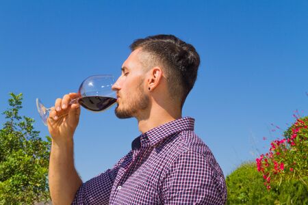 Young farmer tastes a glass of red wine in the vineyard.の写真素材