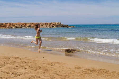 Gorgeous young busty long haired brunette teenage girl in swimswear enjoying jogging at the beach in the summer.の写真素材