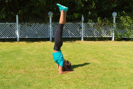 Young slim athletic woman in sportswear, doing handstands on the grass in the summer. Healthy lifestyle and fitness concept.の写真素材