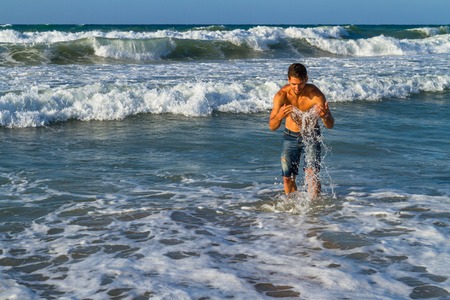 Attractive young man enjoys splashing in the ocean water, in the summer at dusk.の写真素材