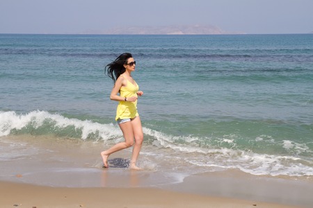 Beautiful long haired woman in beachwear and sunglasses enjoying jogging at the beach in the summer.の写真素材