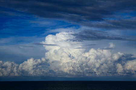 Panoramic view of ocean waters horizon line with dramatic cumulus thunderstorm cloudscape in blue sky background.の写真素材