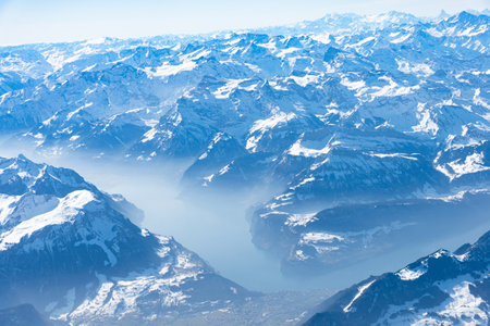 Blue planet earth unique alpine aerial panorama. High altitude aerial view of snow capped central European Swiiss Alps lakes, seen from an airplane cabin window. Enviromental conservation concept.の写真素材