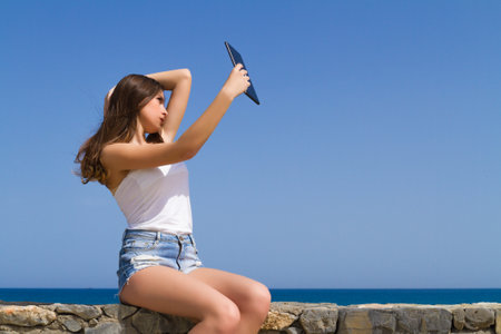 Beautiful teenage brunette teen in jean shorts using a tablet.の写真素材