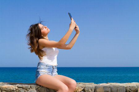 Beautiful teenage brunette teen in jean shorts using a tablet.の写真素材