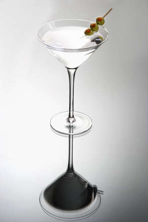 Martini mixed drink with olive garnish on a light grey background with reflectionの写真素材
