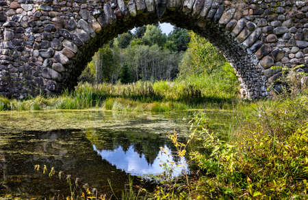 Old stone bridge arch with a reflection of the sky. Vasilevo manor