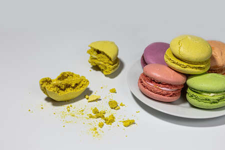 Colorful macaroon cookies on a plate on a white background. Broken yellow cookies into two pieces. Dessert.の写真素材