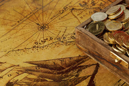 The coins are yellow in a wooden antique chest on an old world map. Journey.の写真素材
