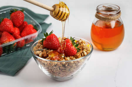 Muesli with strawberries and honey in a glass plate, isolated on a white background. A honey stick.の写真素材