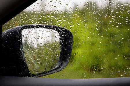View of the side window and rearview mirror from the car interior in the forest. Raindrops on the glass and mirror.の写真素材