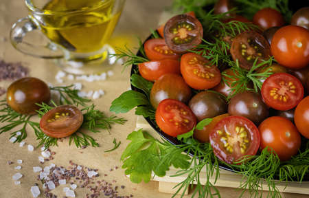 Fresh red and burgundy Cherry tomatoes on a black plate on the table with dill and parsley. Blue Persian and black Indian salt are scattered on the table.の写真素材
