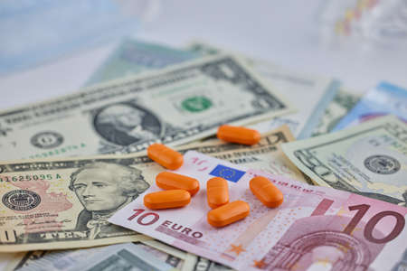 The tablets are orange against the background of dollar and euro banknotes . Pharmacology in the countries of the world.の写真素材