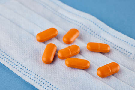Protective face mask, orange pills on a blue background. The concept of the disease.の写真素材