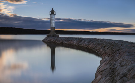 Lighthouse on the stone pier of the lake at sunset against the background of dark clouds. Russia, Karelia.の写真素材