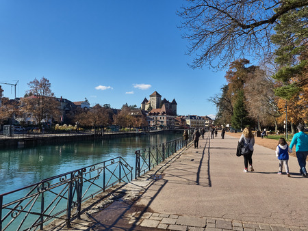 Annecy, France - December 07, 2018: View of the river "Le Thiou", an effluent of the lake of Annecy, and the Castle in the background. The river runs along the "Jardins de l'Europe", the famous garden in Annecy. People are relaxing during the sunny dayのeditorial素材