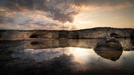 Shot of the sun rising behind the rocks at Cirica Bay at sunrise. Cirica is a beautiful natual seaside place made of cliffs, rocks and sand in the southern Sicily, Italyの写真素材