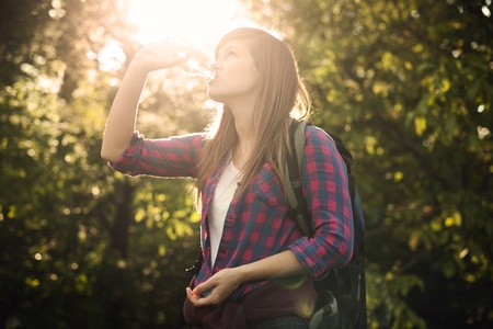 Beautiful female hiker drinking water in forest at sunsetの写真素材