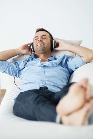 Cheerful man wearing headphones lying on the sofaの写真素材