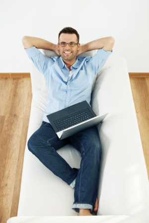 Man relaxing on sofa with laptop and hand behind headの写真素材