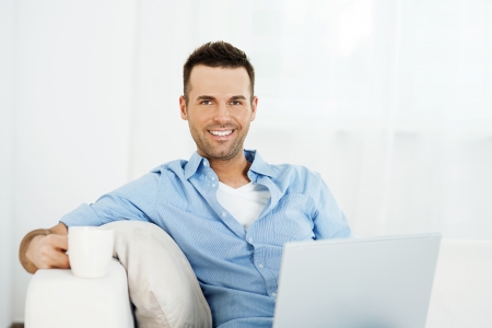 Cheerful man relaxing with laptop and cup of coffeeの写真素材