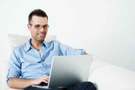 Handsome man in glasses using laptop on sofaの写真素材