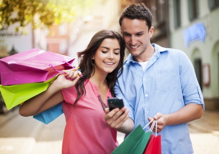Young couple with shopping bag using mobile phone の写真素材