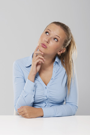 Thinking and pensive woman sitting at white desk の写真素材