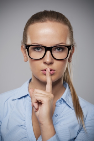 Serious woman wearing glasses showing quiet hand signの写真素材