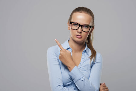 Serious woman wearing fashion glasses pointing at copy space の写真素材