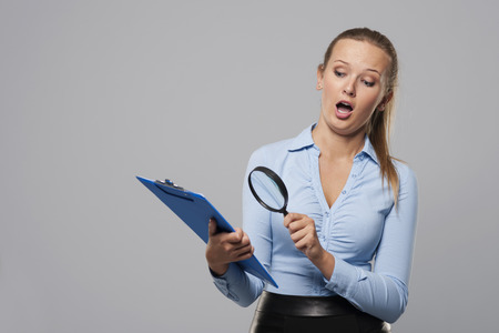 Shocked woman looking at office documents with magnifierの写真素材